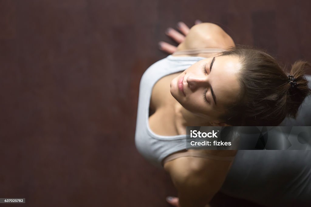 Top view of upward facing dog or cobra yoga pose Beautiful young happy model girl working out in home interior, doing yoga exercise on wooden floor, stretching in upward facing dog or cobra pose. High angle view. Copy space Yoga Stock Photo