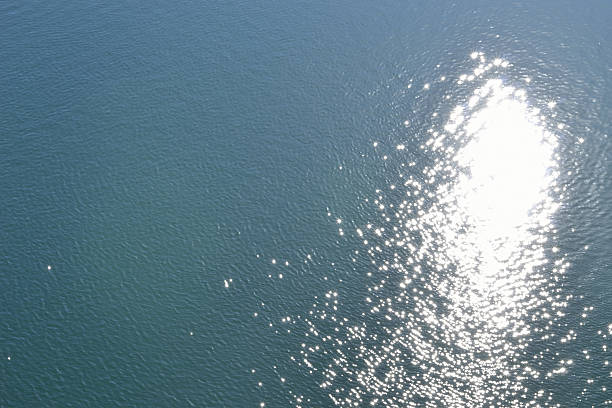 Brilliant gold lens flare on textured ripples on ocean surface reflecting the sunrise. Photographed in Western Australia.