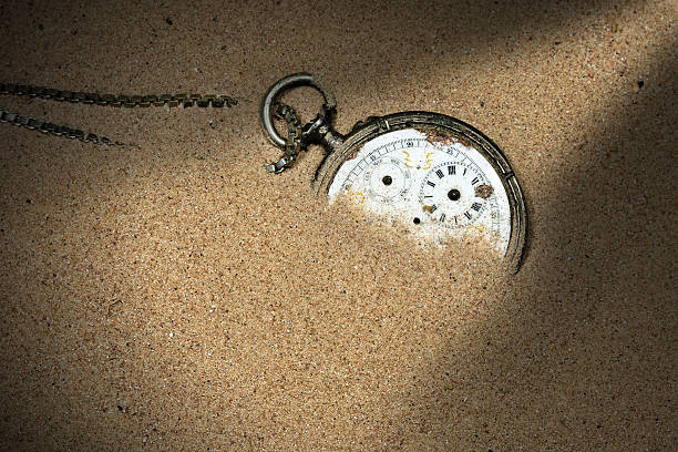 Broken Pocket Watch in the Sand Old and broken pocket watch with chain and without watch hands partially buried in the sand broken pocket watch stock pictures, royalty-free photos & images