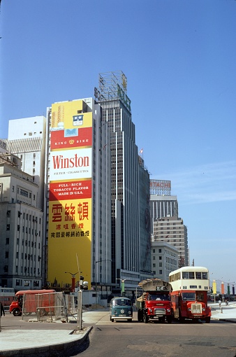 Hong Kong, Special Administrative Region of the People's Republic of China, June 2, 1976. The former British crown colony was returned to China in 1997. Hong Kong is now officially a part of China with special rights. The Connaught Road Central. There are three vehicles at a traffic light. In the background advertising at high-rise facades.