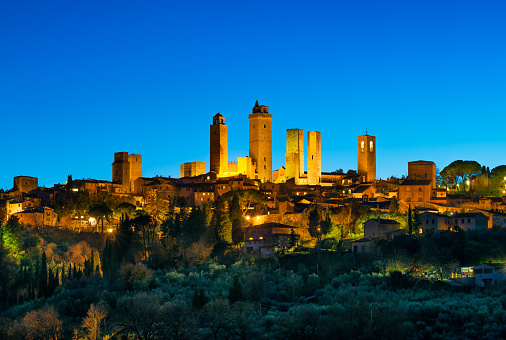 San Gimignano town skyline and medieval towers sunset in blue hour. Italian olive trees in foreground. Tuscany, Italy, Europe.