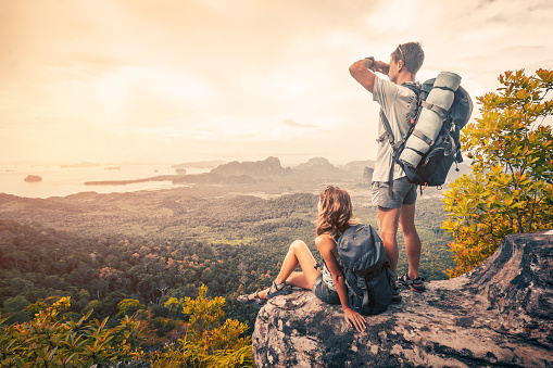 Couple of tourist with backpacks relaxing on top of a mountain and enjoying the view of valley