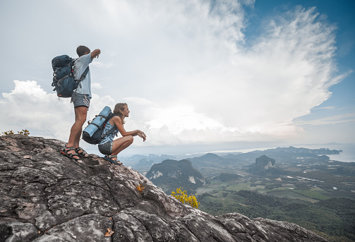 Hikers with backpacks relaxing on top of a mountain and enjoying the view of valley