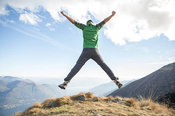 Young hiking man at the top of a mountain jumping high up for success. Swiss Alps and lake on the background. Autumn season.