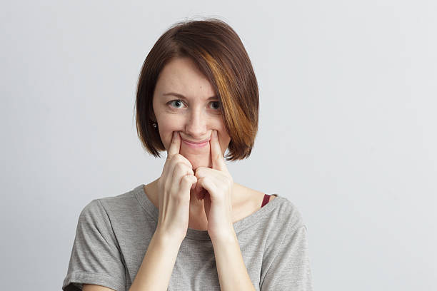 Girl tries to pull smile with fingers over her mouth. Girl tries to pull a smile with fingers over her mouth. Sad mood and pretense. cheesy grin photos stock pictures, royalty-free photos & images
