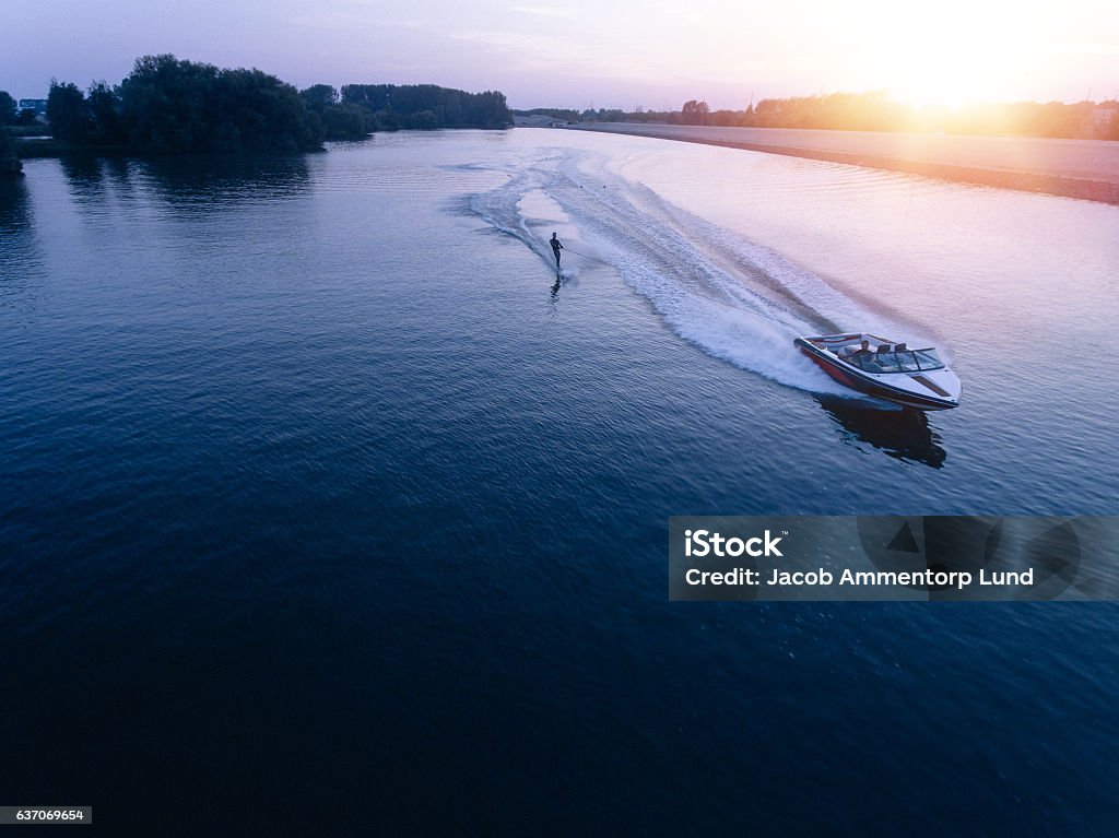 Man water skiiing on lake behind a boat Aerial view of man wakeboarding on lake at sunset. Water skiing on lake behind a boat. Nautical Vessel Stock Photo