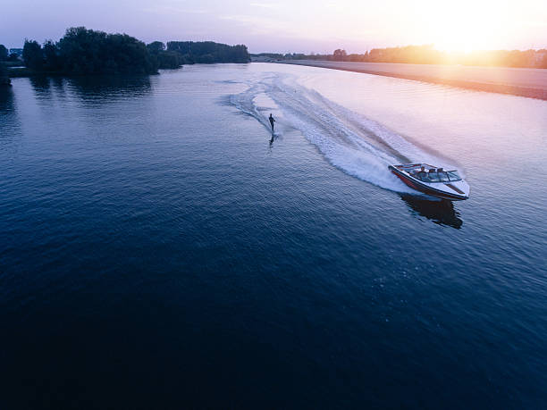 Man water skiiing on lake behind a boat Aerial view of man wakeboarding on lake at sunset. Water skiing on lake behind a boat. towing photos stock pictures, royalty-free photos & images