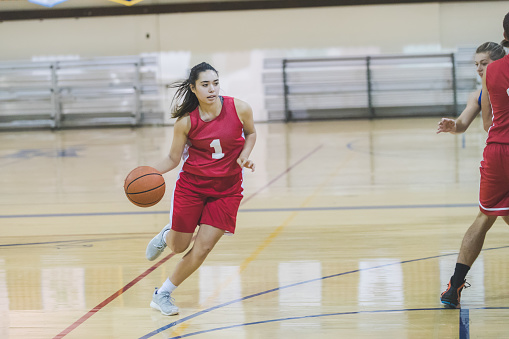 A teenage female basketball player is driving to the hoop during a competitive game