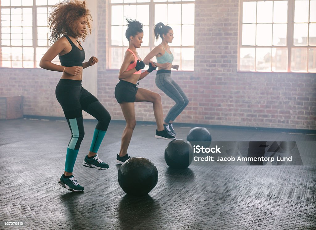 Women exercising in aerobics class Young women exercising in aerobics class with medicine balls on floor. Three females doing workout together in gym. Exercise Class Stock Photo