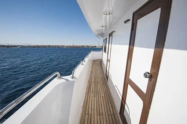 View along gangway down side of a large private motor yacht under way sailing out on tropical sea
