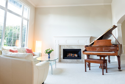 Bright day light coming into living room with burning fireplace, grand piano and white leather sofa.