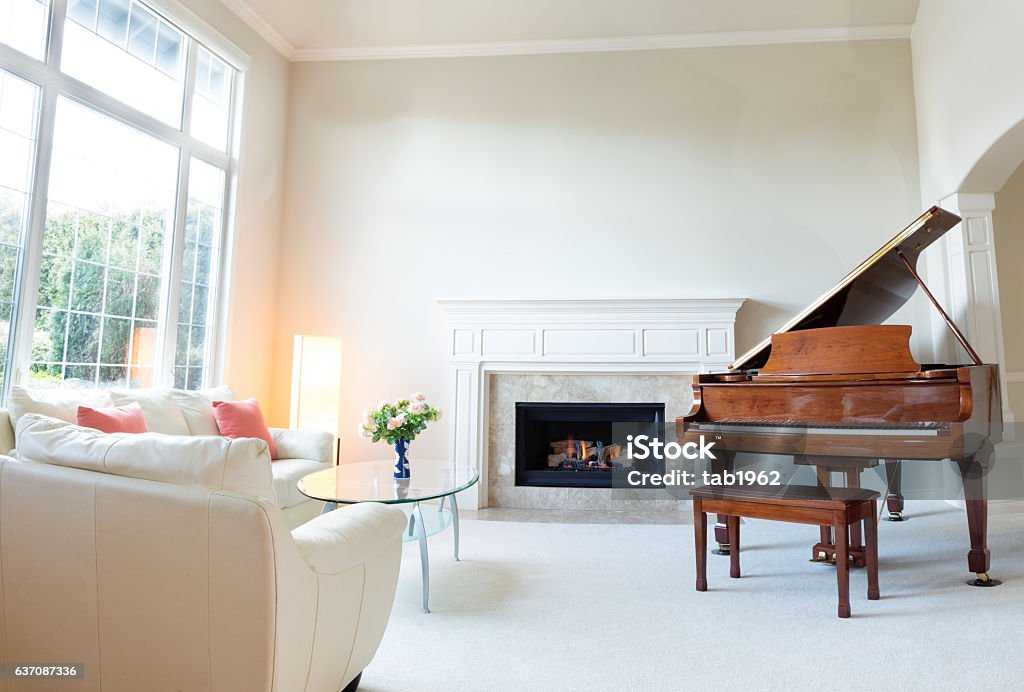 Living room decorated with leather sofa and piano Bright day light coming into living room with burning fireplace, grand piano and white leather sofa. Piano Stock Photo