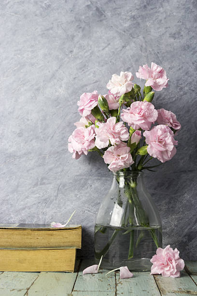 istock Pink carnation flowers in clear bottle and old book 637099982