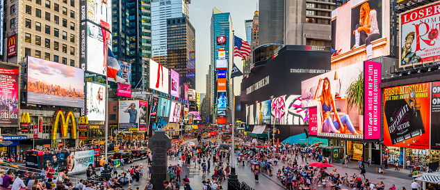 New York City, USA - August 20, 2015: Times Square panorama taken on a busy evening in New York. Like usual there is a lot of people walking around and the image contains visual commercials of multiple companies. There is also a flag of the USA in the middle of the image.