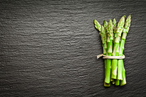 Tied up fresh organic bunch of tender asparagus shot from above on dark slate background. The bunch is placed at the right side of the frame leaving a useful copy space in the frame. DSRL studio photo taken with Canon EOS 5D Mk II and Canon EF 100mm f/2.8L Macro IS USM