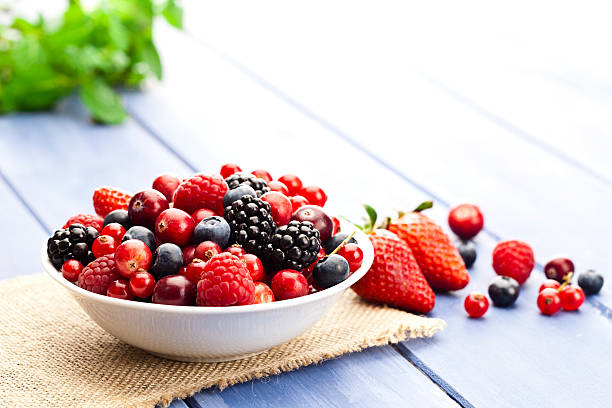 Mixed organic berries White bowl filled with fresh mixed organic berries on blue garden table. Some berries are scattered outside the bowl. DSRL studio photo taken with Canon EOS 5D Mk II and Canon EF 100mm f/2.8L Macro IS USM berry fruit stock pictures, royalty-free photos & images