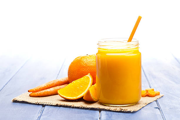 Glass jar with orange and carrot juice on blue table. Predominant colors are orange and blue.  DSRL studio photo taken with Canon EOS 5D Mk II and Canon EF100mm f/2.8L Macro IS USM Lens