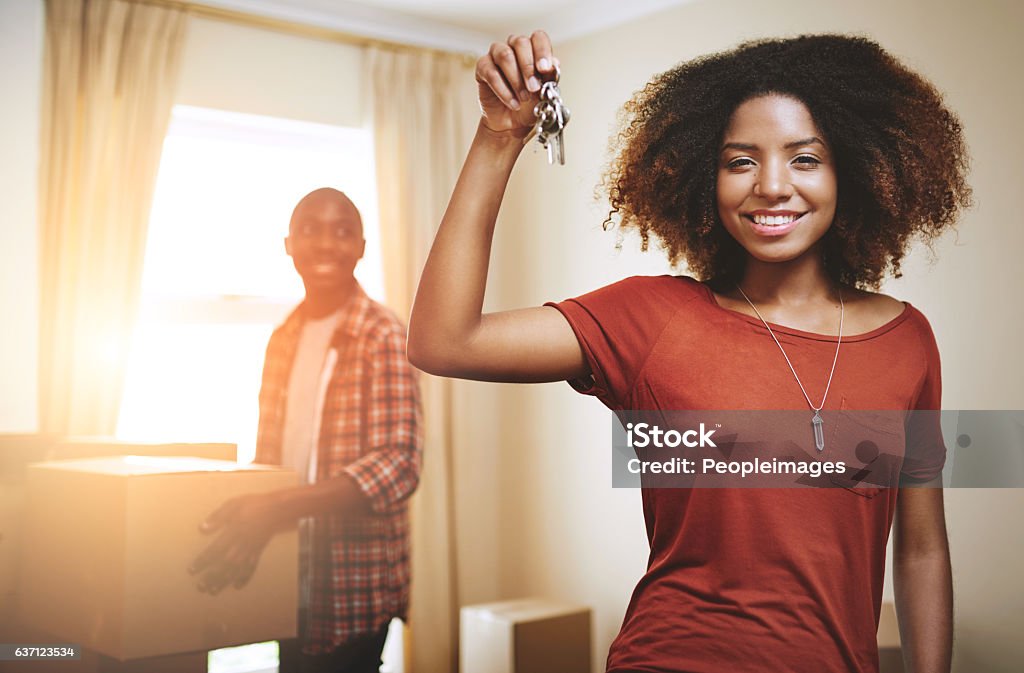 We're finally the owners of our dream house! Portrait of a young woman holding up the keys to a new home with her boyfriend in the background Key Stock Photo