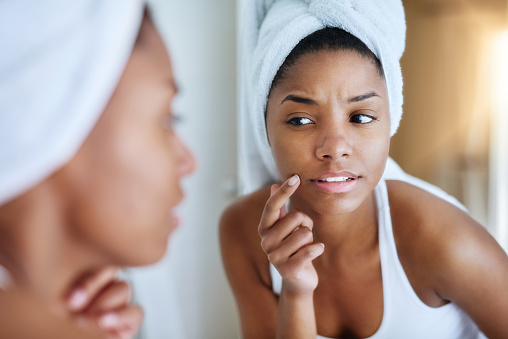 Shot of a young woman inspecting her skin in front of the bathroom mirror and looking upset
