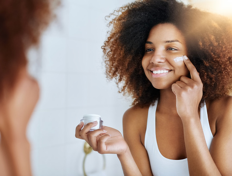 Shot of an attractive young woman applying moisturizer to her face in front of the mirror