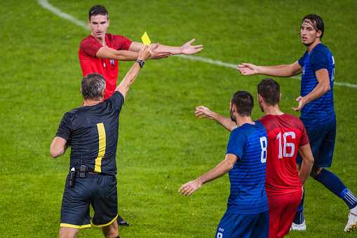 Referee holds up yellow card and showing to football players during football match.