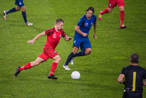 Male football players challenging for ball on field during match.