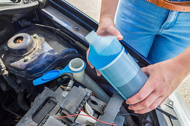 Woman filling car reservoir with blue fluid in bottle Woman filling car reservoir with windshield wiper fluid. This liquid  will clean the wind shield of this vehicle. That will guarantee a clear window with excellent sight. The european teenage girl is eighteen years old and as a driver she cares for her vehicle. liquid battery stock pictures, royalty-free photos & images