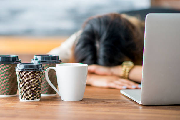 Tired Entrepreneur A female entrepreneur and businesswoman is working on her start up company in her office. She has fallen asleep at the office with her head on her desk. Empty coffee cups are on the table. exhaustion stock pictures, royalty-free photos & images