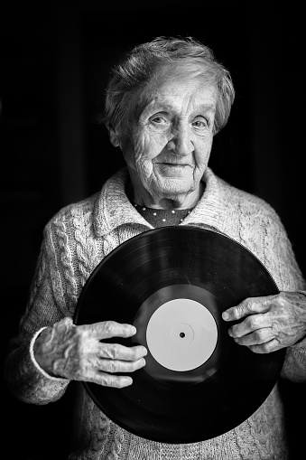 Elderly woman is holding a vinyl record. Black and white photo.