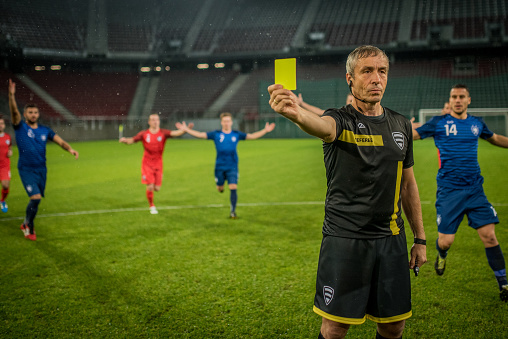 Referee holds up yellow card during football match.