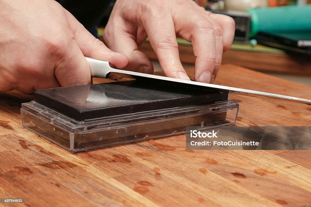 Sharpening knife. Close up of man sharpening knife on whetstone. Hands of chef using grindstone for sharpening knife edge. Adult Stock Photo