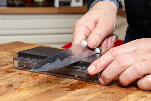 Close up of hands sharpening knife edge on grindstone. Man using whetstone.