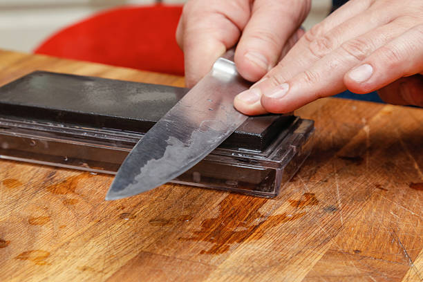 Man sharpening knife. Sharpening knife on sharpening stone. Close up of man using whetstone for sharpening knife blade. blade stock pictures, royalty-free photos & images