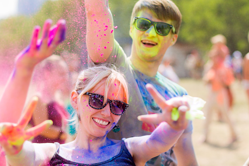 Girl and guy wearing sunglasses having fun during Holifest throwing colorful powder in the air