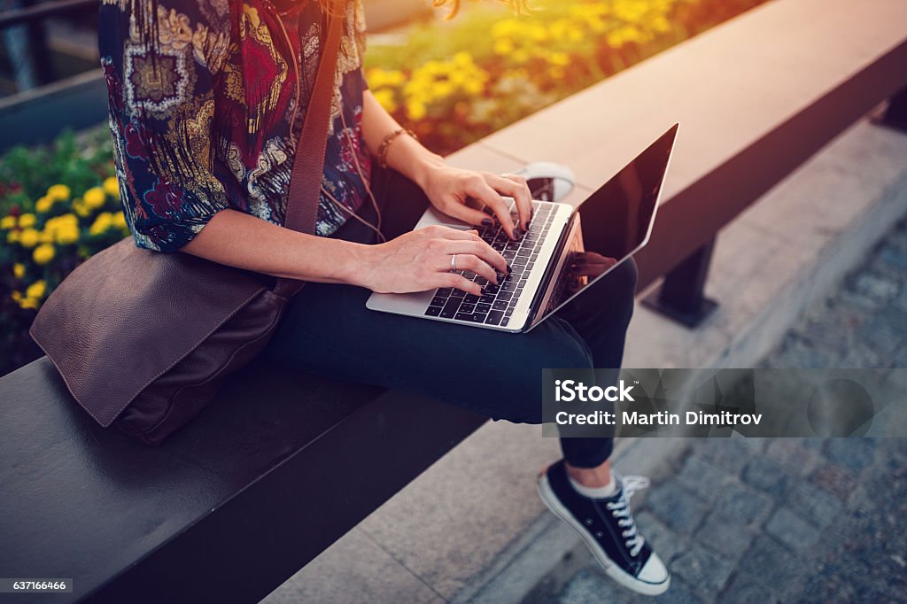 Teenage girl using lap top at the bridge Young woman working from computer in the city park Outdoors Stock Photo