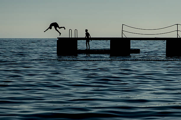 istock Silhouette of two boys, one diving off jetty 637169198