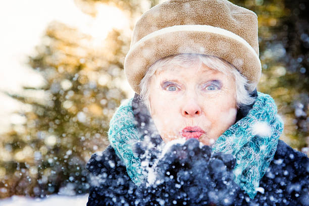 Senior woman blowing snow  to camera sunset forest Canada stock photo