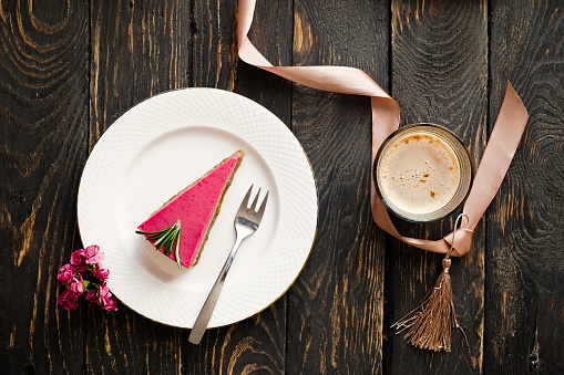 Heart shaped ribbon, coffee and raspberry cake slice. Valentine's day dessert. Dark wooden table