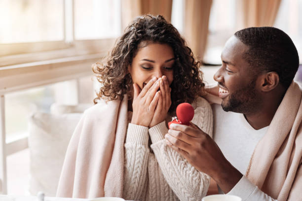 Amazed African American couple getting engaged in the cafe I love you. Amazed surprised positive African American couple sitting in the cafe and being covered with a blanket while getting engaged ring jewelry photos stock pictures, royalty-free photos & images