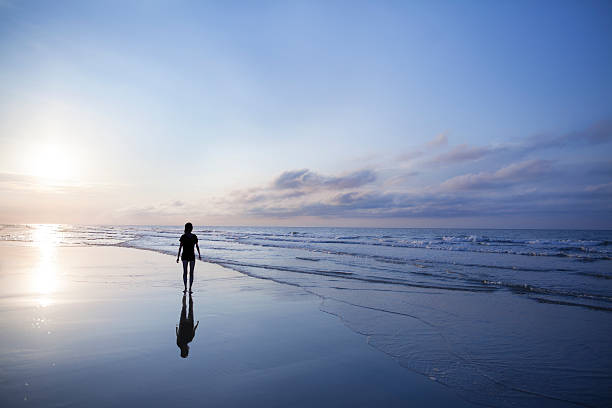 femme marchant sur la plage au lever du soleil - vanishing view photos et images de collection