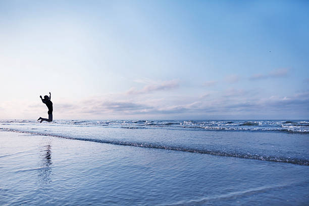 mujer saltando de alegría en la playa al amanecer - beach sea zen like nature fotografías e imágenes de stock