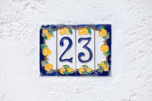 Colorful earthenware plate with a number 23 in its middle. The plate is stuck on the white wall of a front