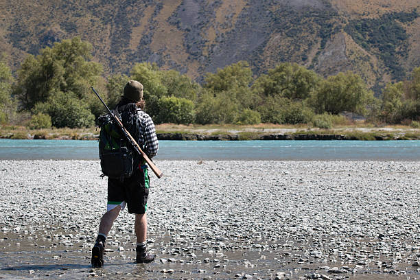 Kiwi hunter Young hunter with a rifle crossing mountain river, New Zealand high country stock pictures, royalty-free photos & images