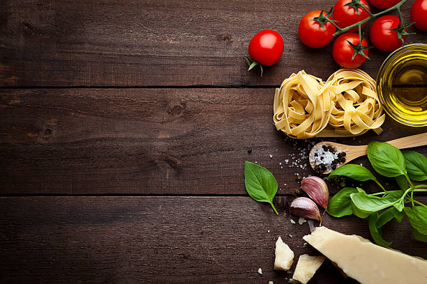 Pasta ingredients Ingredients for cooking traditional italian pasta shot on rustic wood table. The ingredient are paced at the right side of the frame leaving a useful copy space at the center-left side. Composition includes tagliatelle pasta, olive oil, tomatoes, basil, pepper, salt, garlic and parmesan cheese. Low key DSRL studio photo taken with Canon EOS 5D Mk II and Canon EF 100mm f/2.8L Macro IS USM italian food stock pictures, royalty-free photos & images