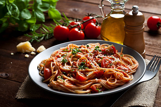 Pasta plate Pasta with tomato sauce shot on rustic wood table. Some ingredients for cooking pasta like tomatoes, olive oil, basil, parmesan cheese and a pepper mill are around the plate. DSRL low key studio photo taken with Canon EOS 5D Mk II and Canon EF 100mm f/2.8L Macro IS USM italian food stock pictures, royalty-free photos & images