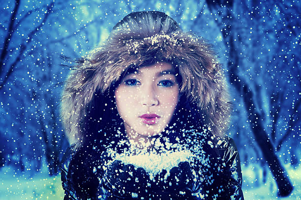 Teenage girl wearing winter clothes and blowing snow on her hands at the park