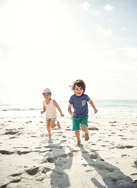 Did someone say ice cream? Portrait of two young siblings running on the beach happy sibling day stock pictures, royalty-free photos & images