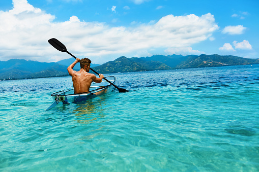 Summer Travel Kayaking. Man Paddling Transparent Canoe Kayak In Tropical Ocean, Enjoying Recreational Sporting Activity. Male Canoeing With Paddle, Exploring Sea On Vacation. Rowing Water Sports