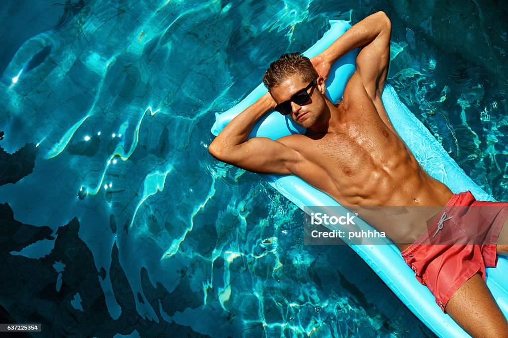 Summer Man Body Care. Beautiful Male Relaxing In Pool Summer Man Body Sun Skin Care. Beautiful Model With Sexy Body In Swimwear Tanning, Floating On Mattress In Swimming Pool Water. Fitness Male With Healthy Tan Relaxing At Relax Spa Resort. Summertime Men Stock Photo