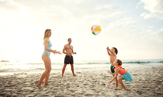 Shot of a family playing catch with a beach ball while enjoying a day at the beach